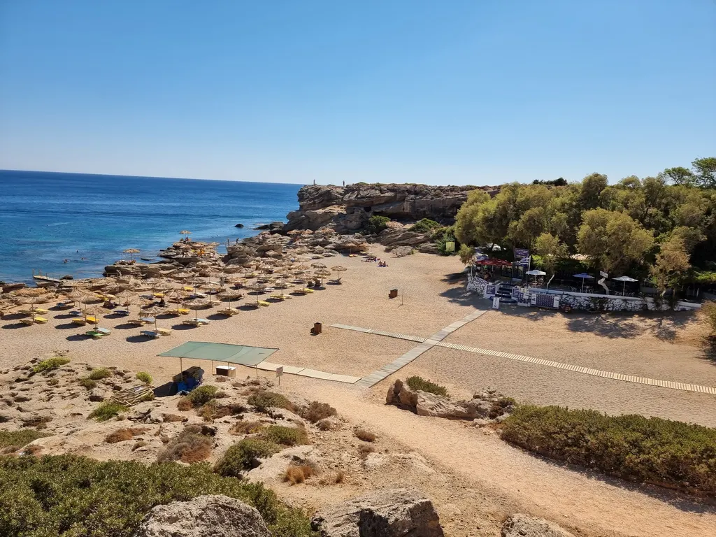 A sandy beach with rows of umbrellas beside clear blue water on the east coast of Rhodes