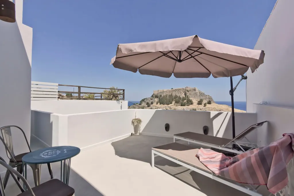 Private terrace of the Honeymoon Suite with sunbeds, an umbrella and a view of the Acropolis of Lindos